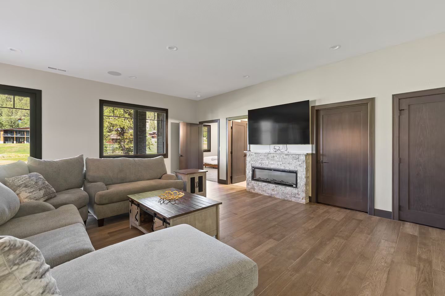 Lower-level family room with a large sectional, a fireplace in a stacked-stone surround and a wall TV