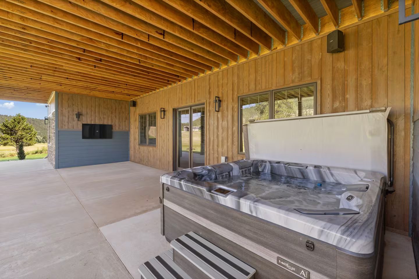 Hot tub on the covered lower patio, with an outdoor TV on the wall and the golf course beyond