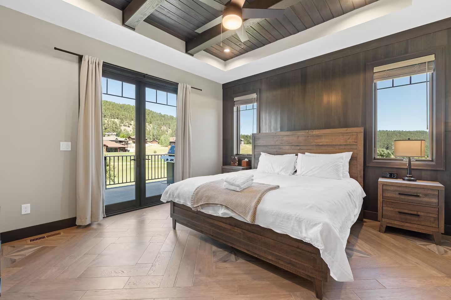 King bedroom with a dark wood accent wall, a coffered wood ceiling, herringbone floors and French doors to the deck