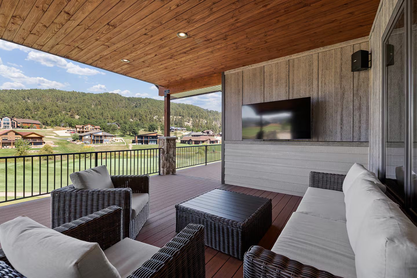 Covered upper deck with wicker lounge seating and a wall-mounted outdoor TV, overlooking the golf course and the Black Hills