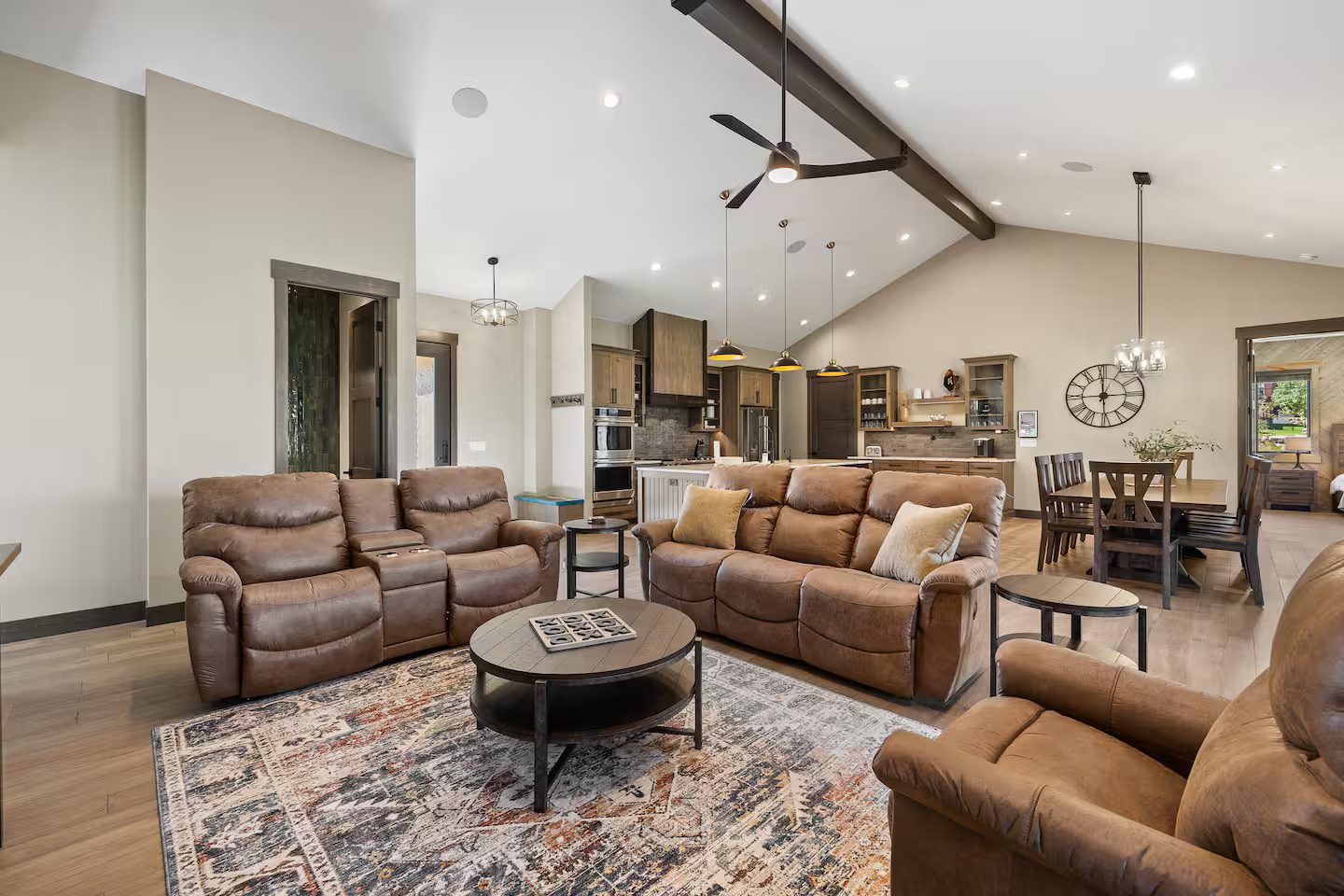 Great room at the Luxury Black Hills Retreat with leather recliners, a vaulted ceiling with a dark wood beam, and the kitchen and dining table beyond