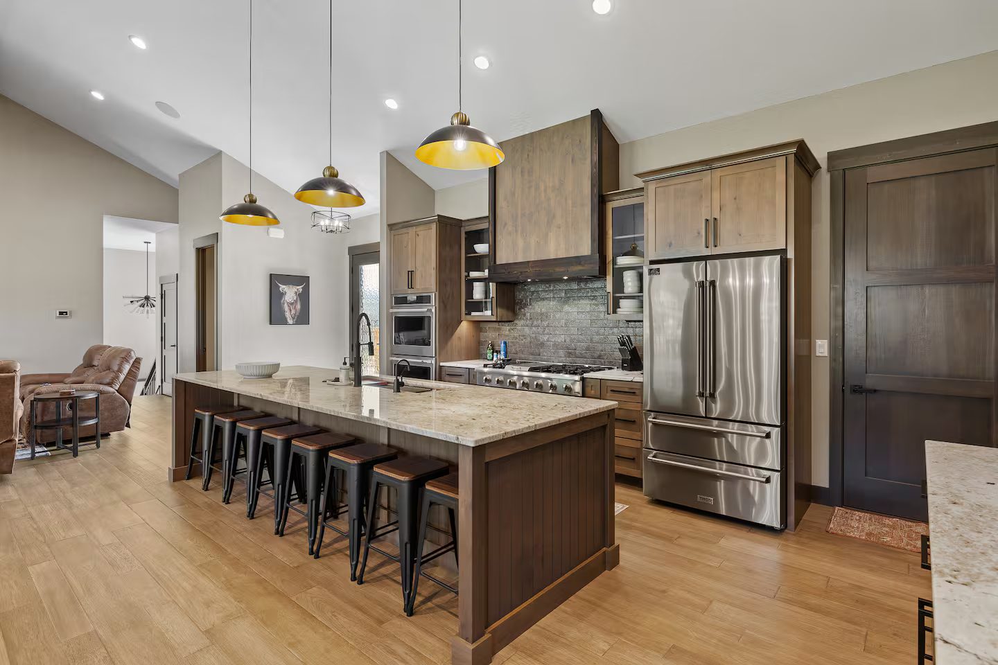 Kitchen island with seating for eight, a six-burner range under a wood hood, and a stainless French-door refrigerator